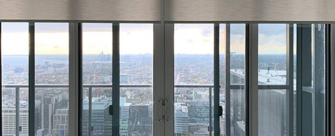 Custom roller blinds on large balcony doors in a Toronto condo with a city view by Nifty Blinds.